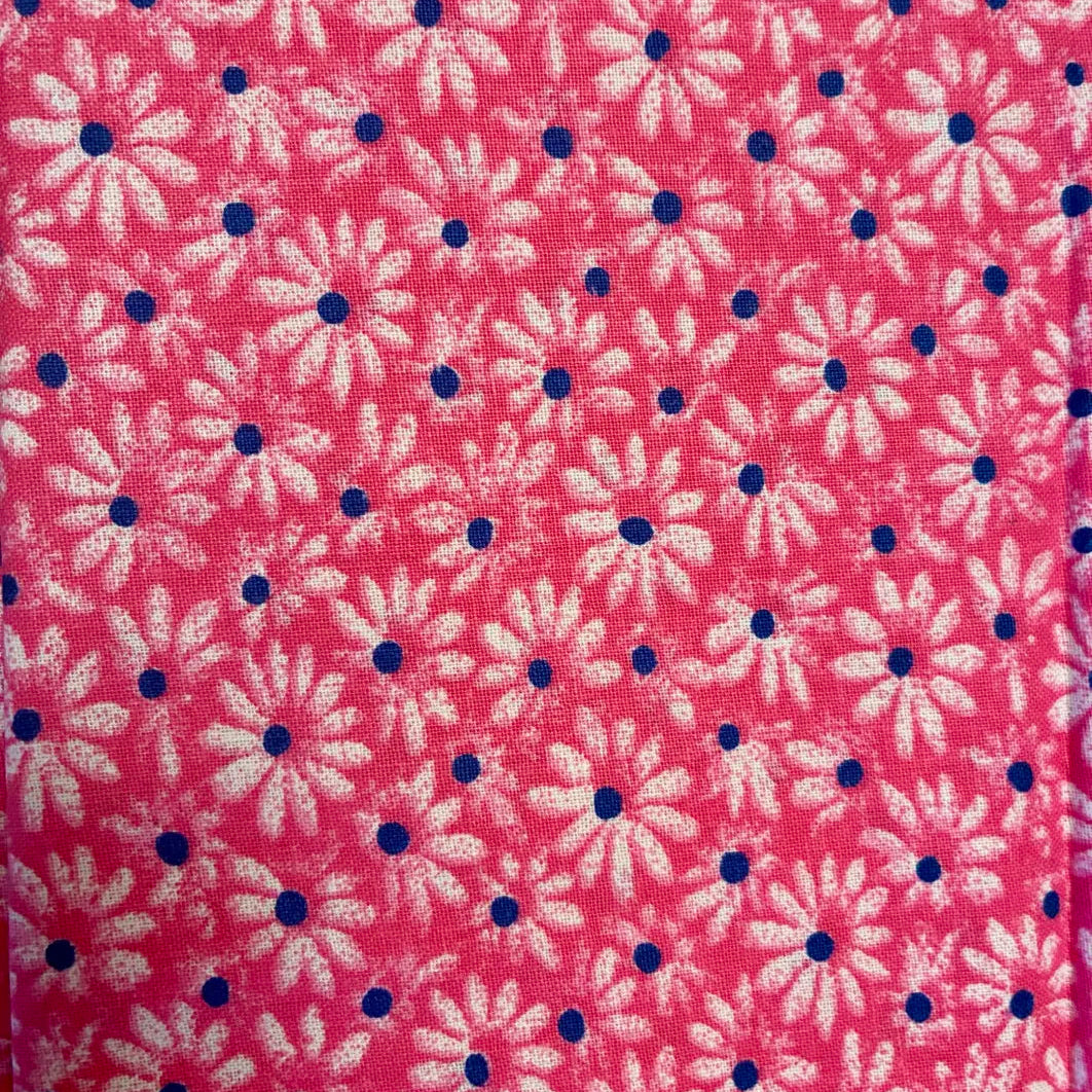 A close-up of a pink fabric with a repeating pattern of white daisy-like flowers and small dark blue dots.