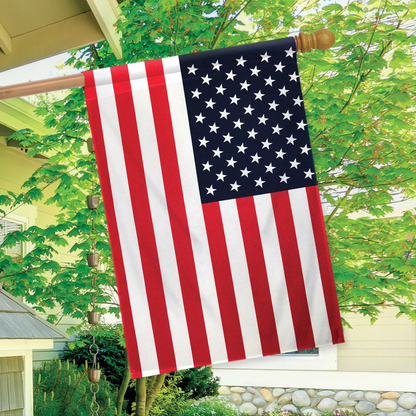 American flag hanging on a pole outdoors with greenery in the background