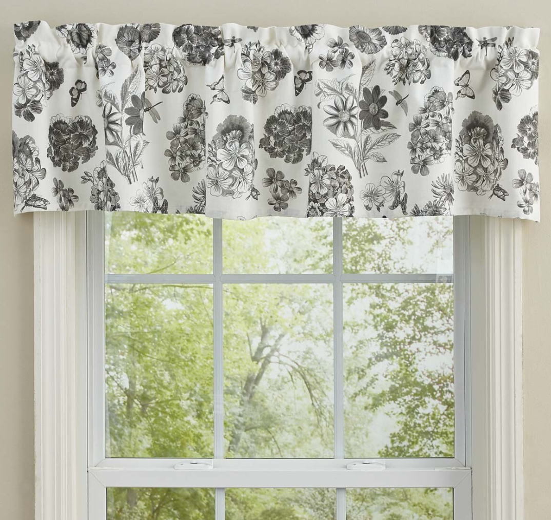Floral patterned curtain valance above a window with greenery outside